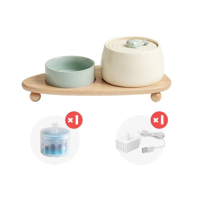 Ceramic set including white cat water fountain with a baby whale motif and a green pet bowl placed on a wooden stand displayed on a white background.