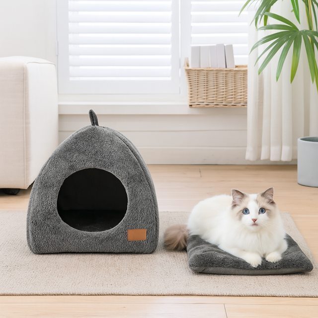 Ragdoll cat laying on a cushion next to a triangle cozy cat cave bed in a bright living room.