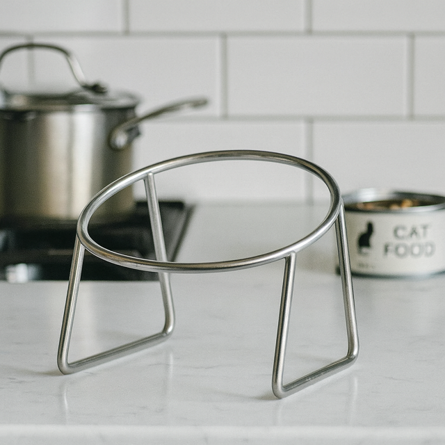 Metal stand supporting stainless steel cat bowl placed on a white marble kitchen bench top.