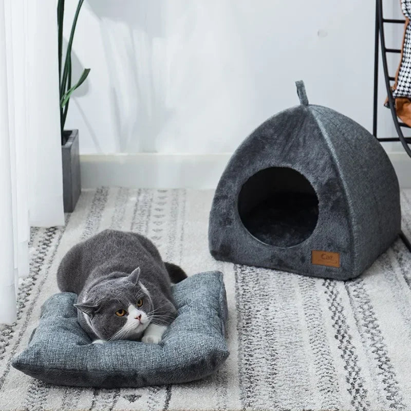 Grey cat laying on a cushion next to a triangular cat cave house.