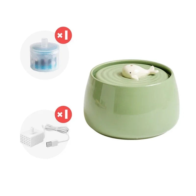 Green ceramic water fountain for cats with a decorative motive of baby whale displayed with USB charger and replacement filter.