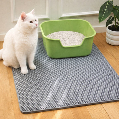 White cat sitting on a grey mat next to a green litter box indoors.