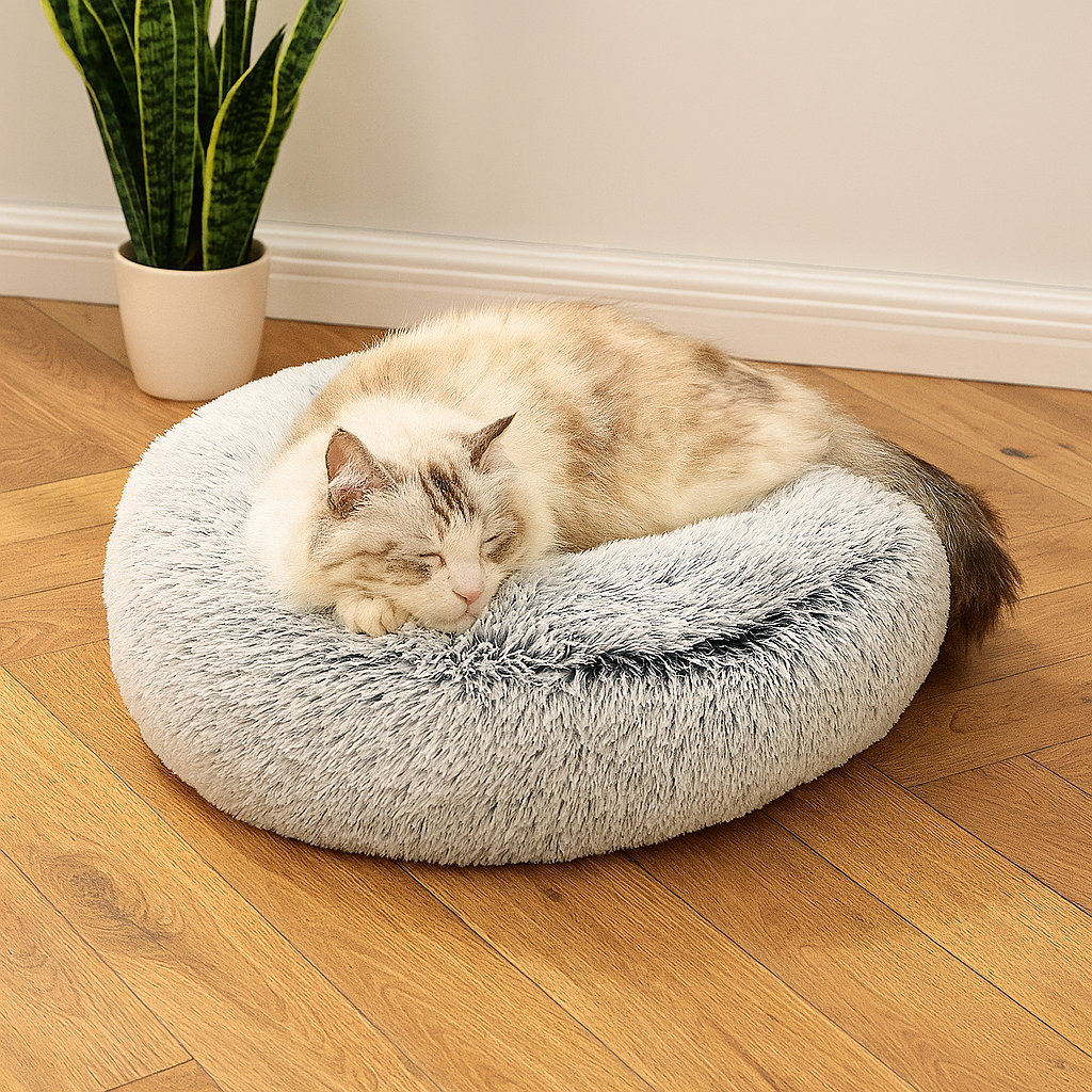 Brown cat sleeps on top of the grey cozy plush cat bed sitting on a wooden floor.