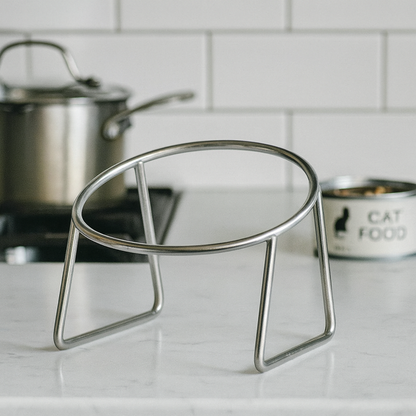 Metal stand supporting stainless steel cat bowl placed on a white marble kitchen bench top.