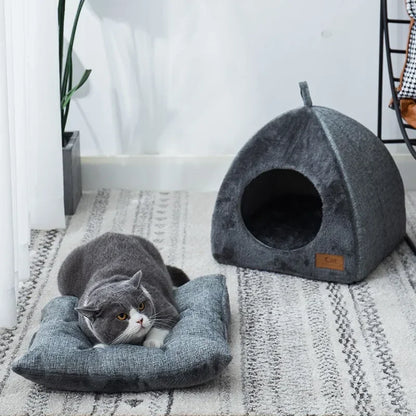 Grey cat laying on a cushion next to a triangular cat cave house.