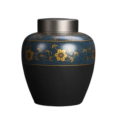 Ceramic black pet cremation urn with a gold and blue ornament displayed on a white background.
